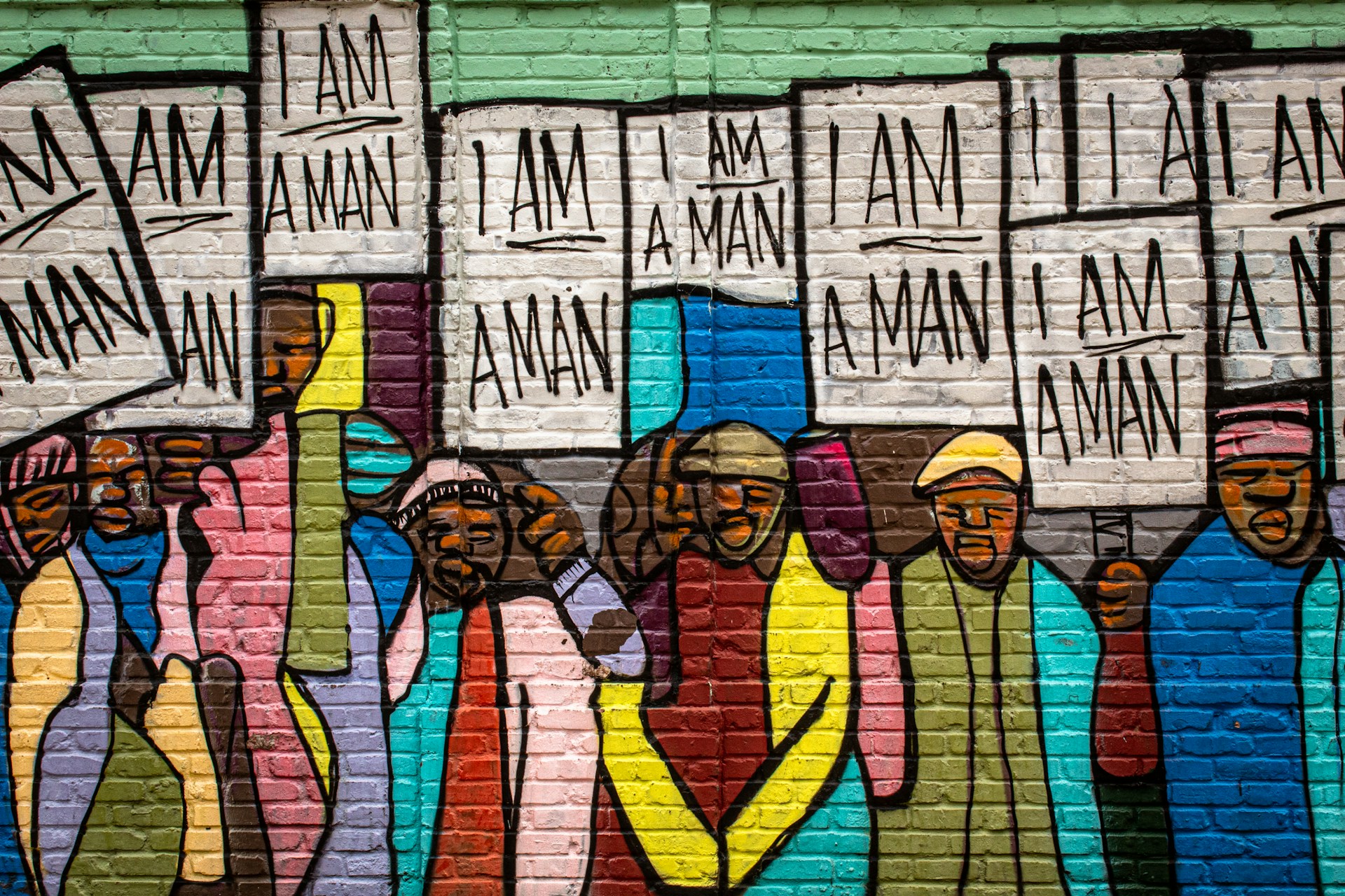 Photo of a mural of black men wearing colorful clothing holding white protest signs that read "I am a man."