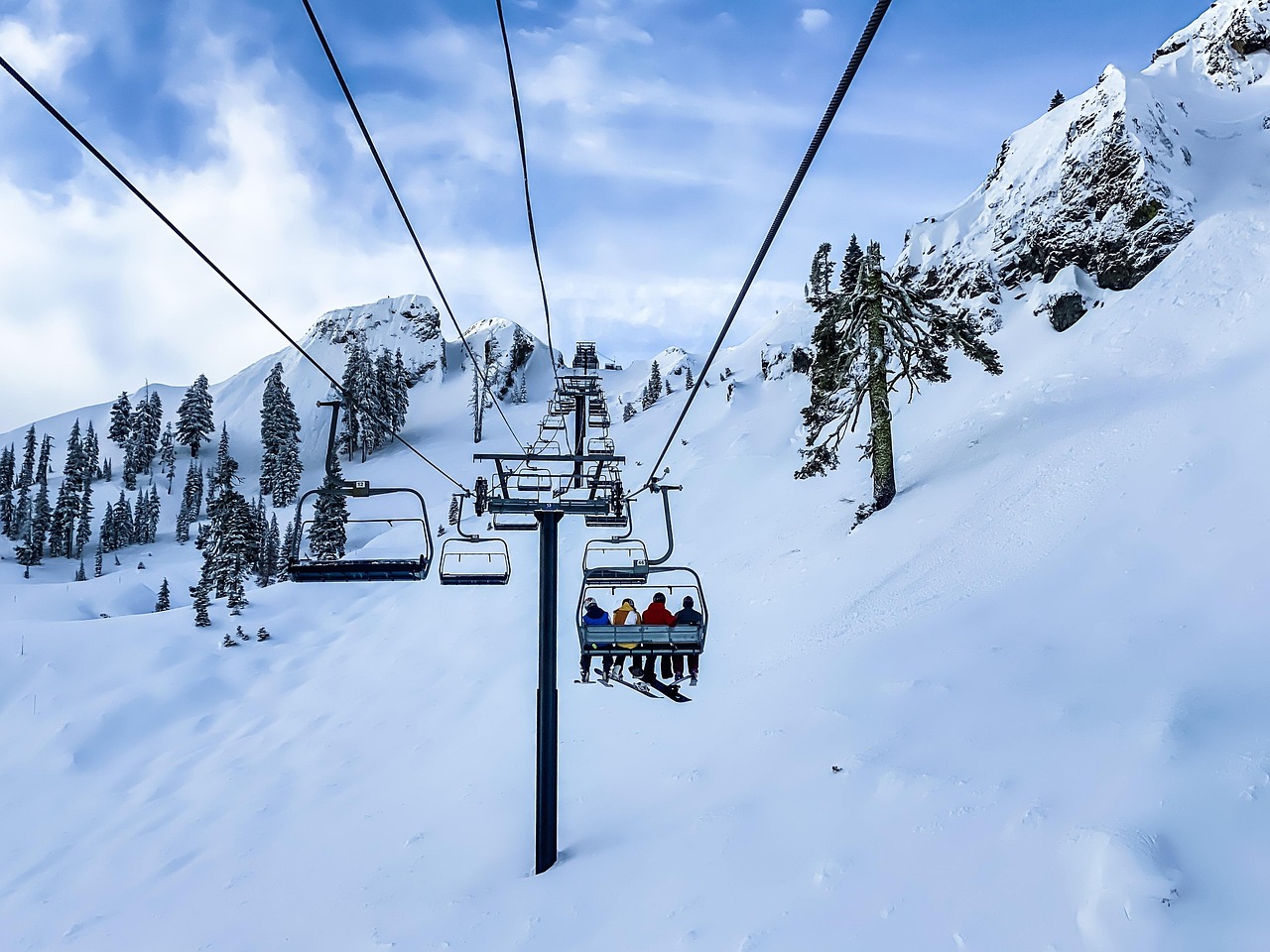 Snowy mountain scene featuring four people riding a ski lift